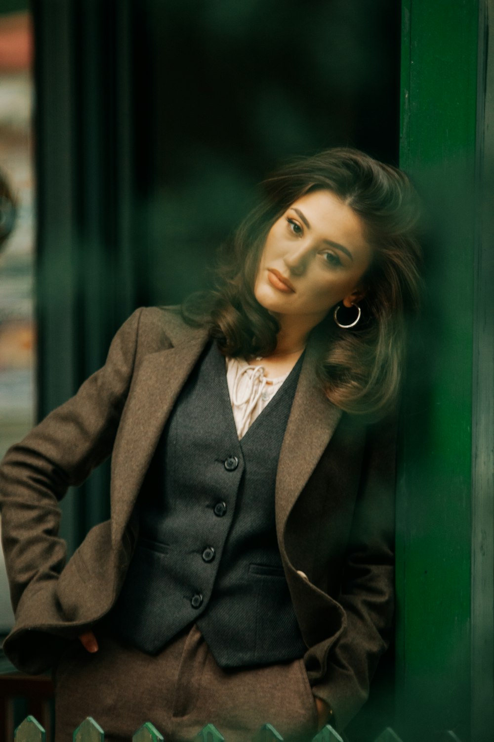 a woman in a suit leaning against a green wall