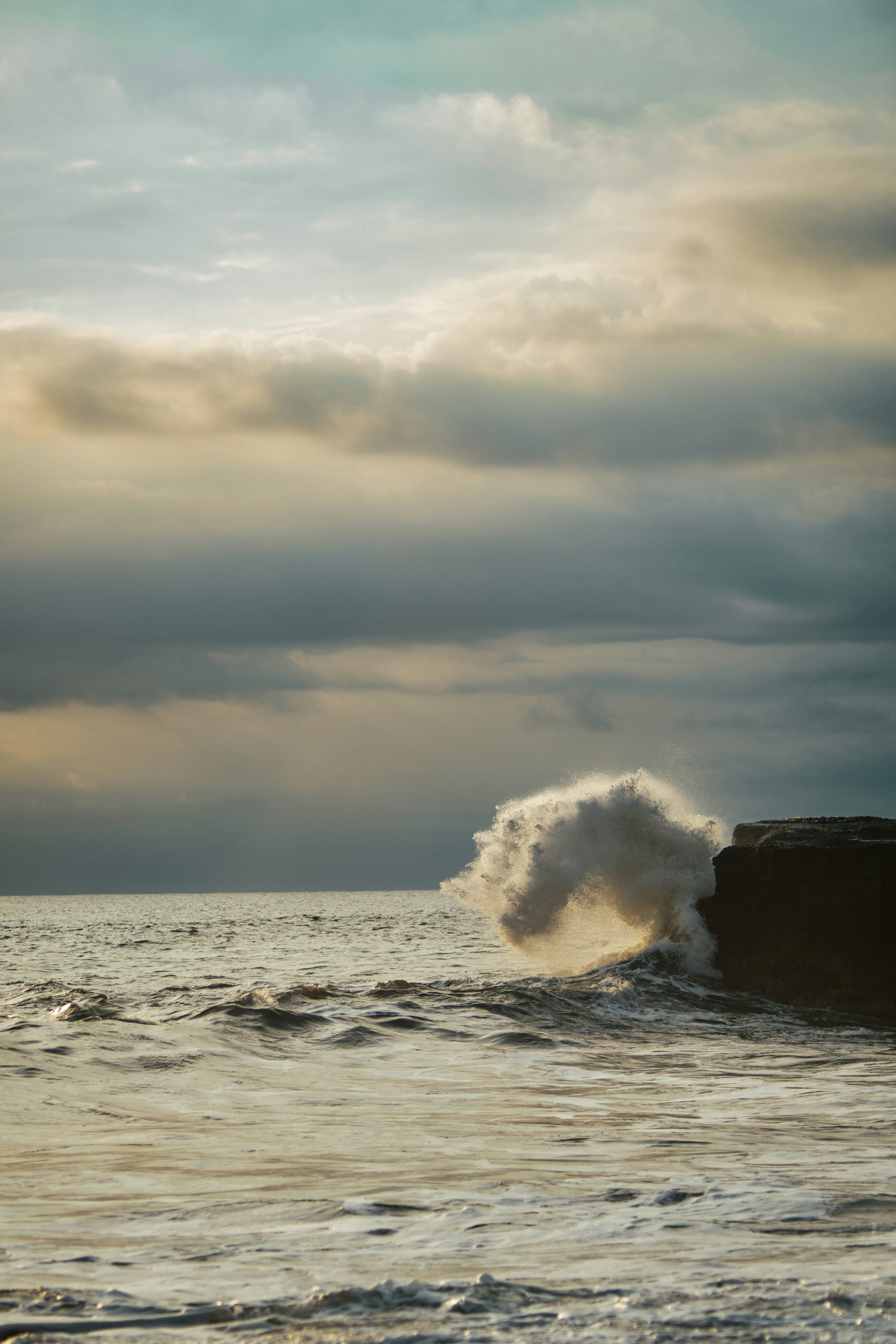 a large wave crashing into the ocean on a cloudy day