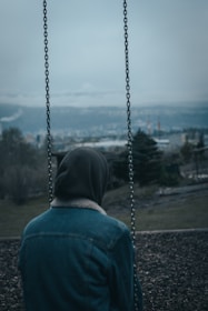 a person sitting on a swing with a hood on