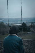 a person sitting on a swing with a hood on