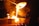 Molten metal is being poured from a large ladle into molds, creating bright orange and yellow flames. Sparks fly as the glowing liquid metal cascades downward, illuminating the surrounding area with intense light.
