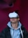 A person wearing a virtual reality headset appears to be engaged or immersed in the experience. They are dressed in a casual outfit consisting of a hoodie and a jacket, with a light-colored background offering a contrast to the darker tones of the clothing.