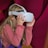 A young girl with long blonde hair is using a white virtual reality headset. She is wearing a long-sleeved, pinkish-red shirt, and appears to be engaged and curious. The background features deep pink and purple colors in a soft, abstract pattern.