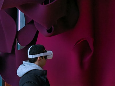 A person is wearing a virtual reality headset, facing a textured, abstract wall with dark maroon and black folds.