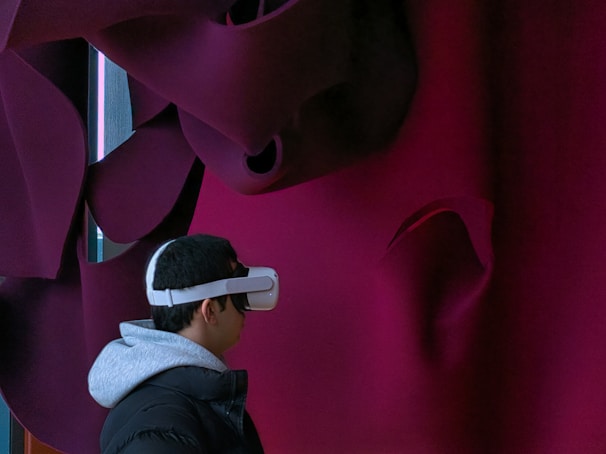 A person is wearing a virtual reality headset, facing a textured, abstract wall with dark maroon and black folds.