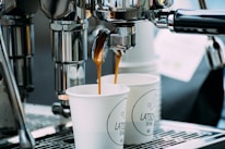 two cups of coffee being poured into a coffee machine