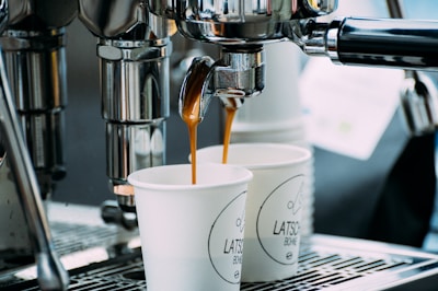 two cups of coffee being poured into a coffee machine