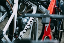 A close-up view of several high-performance racing bicycles oriented tightly together. The image focuses on the frames and wheels, showcasing brand names and sleek designs. There are vibrant colors and elements such as water bottles and intricate handlebar setups.