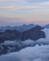 A panoramic view of Mount Rinjani with clouds drifting around its peak.