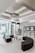 A modern, minimalist waiting room with semi-circular black seating arrangements and glass walls allowing natural light. There are display shelves with books and digital screens on the wall.