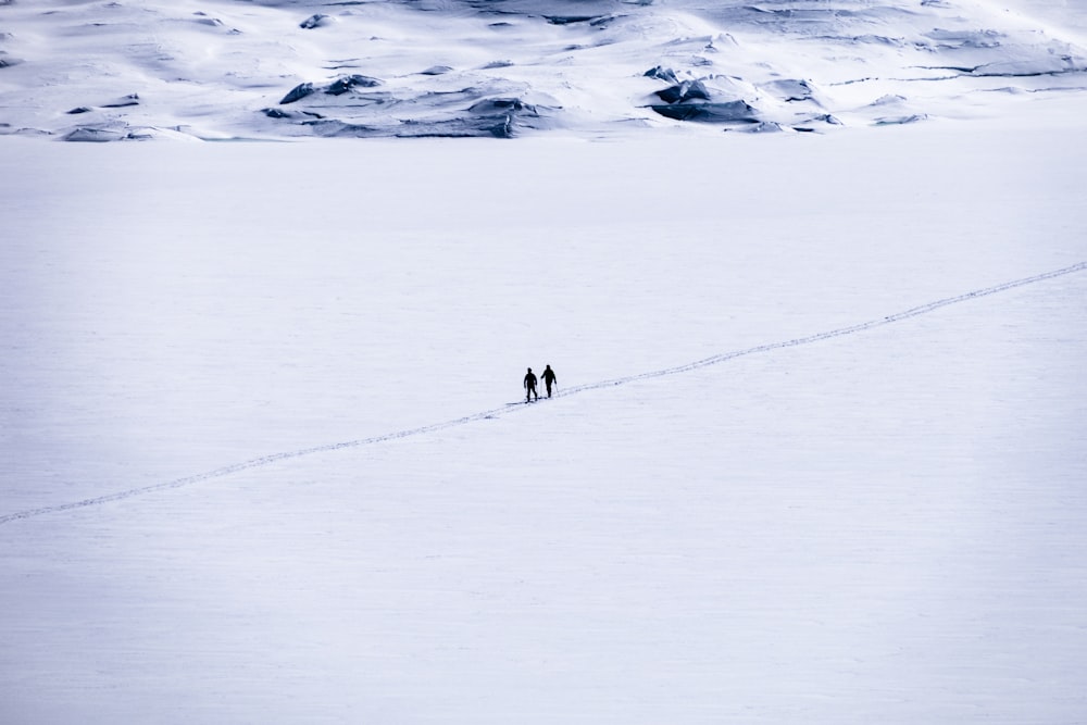 a couple of people walking across a snow covered field