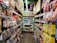 Smiling woman holding a bag of colorful snacks in a bright grocery store aisle.