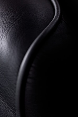 Close-up view of a textured black leather surface with a smooth, curved line running through it, creating a contrast between textures.