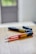 Two auto-injector pens are placed on a wooden surface, with one pen in the foreground having a prominent red and yellow color, while the other pen is blurred in the background.