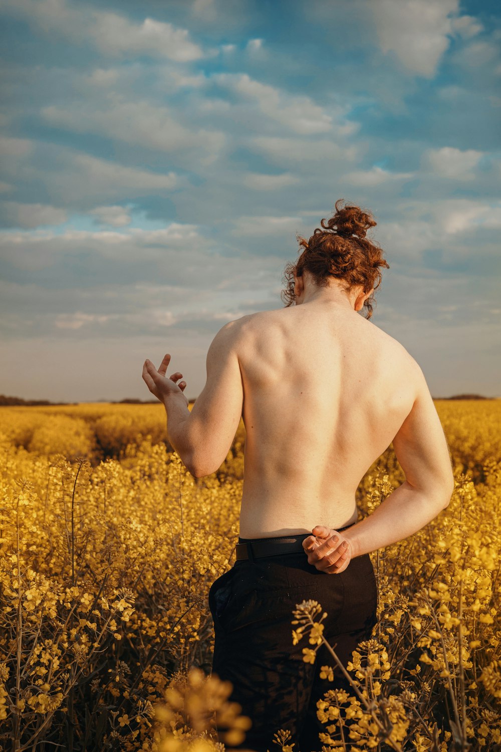 a shirtless man standing in a field of yellow flowers
