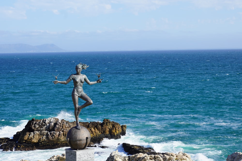 a statue of a woman standing on top of a rock next to the ocean