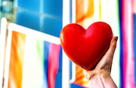 a person holding a red heart in front of a colorful wall
