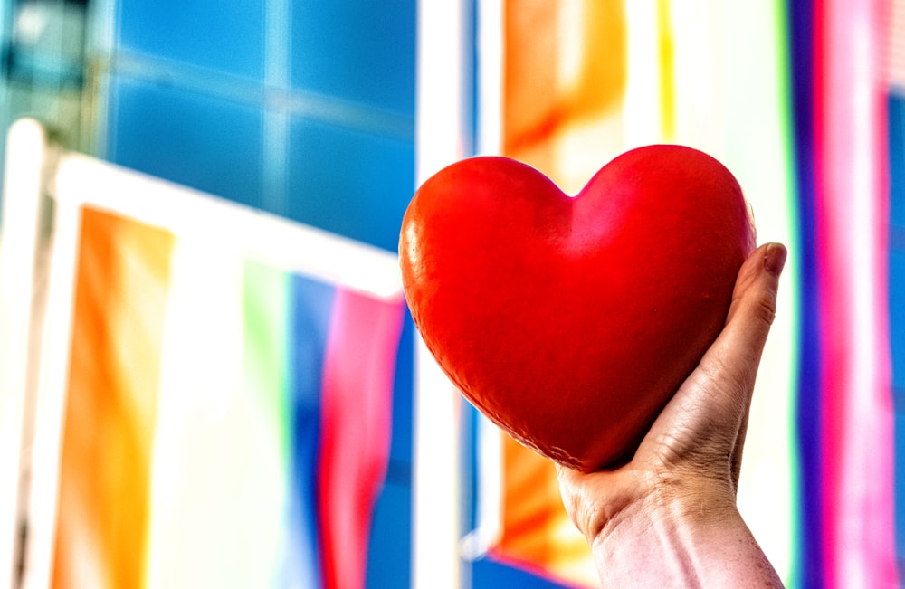 a person holding a red heart in front of a colorful wall