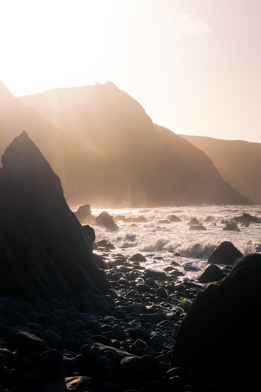 the sun shines on a rocky beach near the ocean