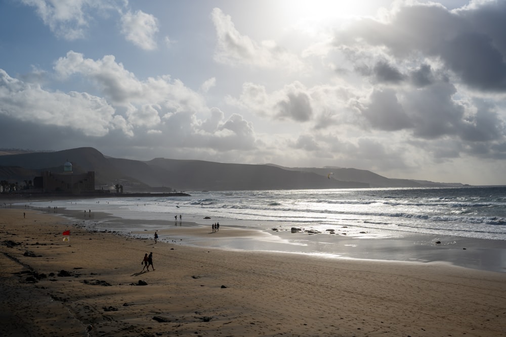 a sandy beach with people walking on it under a cloudy sky