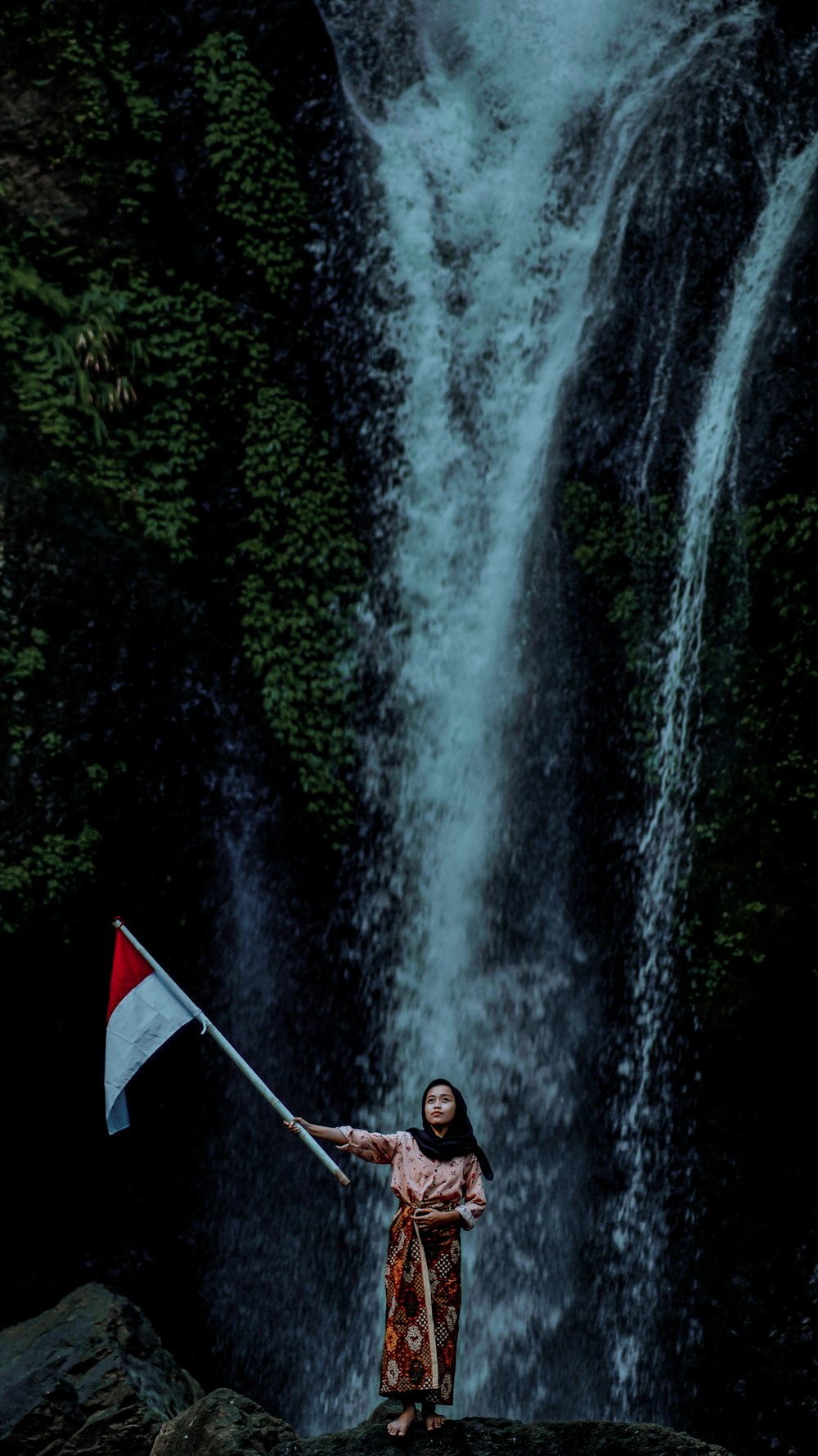 a woman holding a flag standing in front of a waterfall