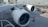 An airplane is parked at an airport with a focus on the two large jet engines prominently displaying a logo. The surrounding area includes tarmac, airport infrastructure, and a few small ground service vehicles.