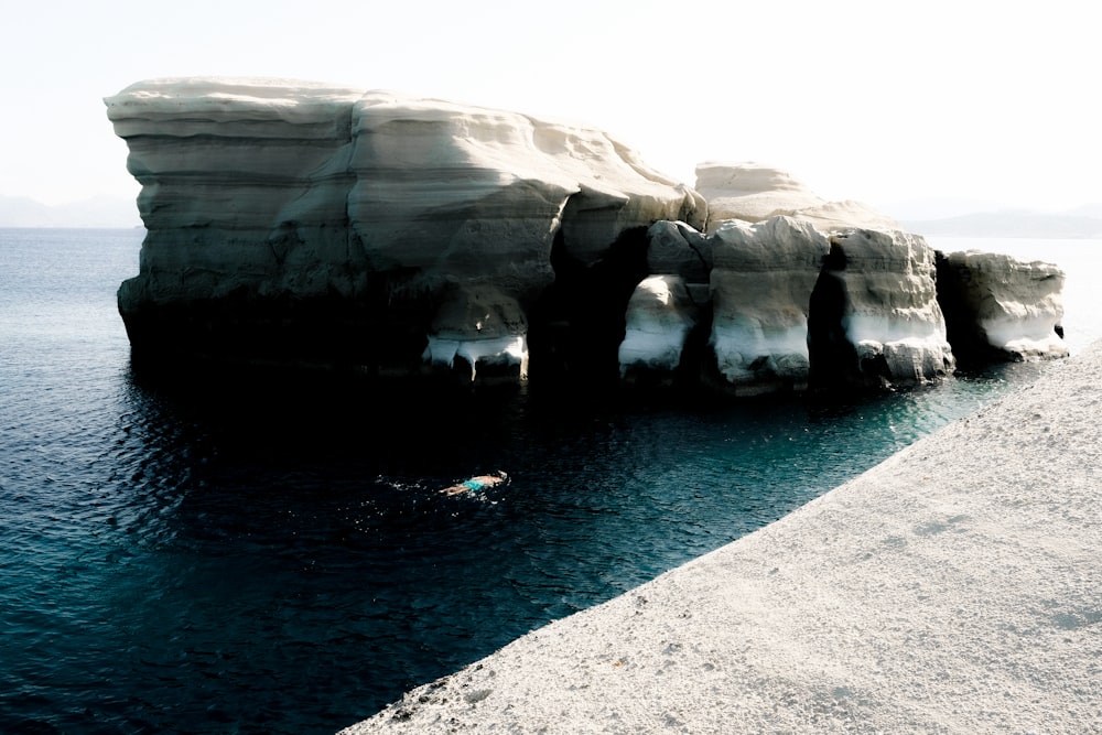 a person swimming in a body of water next to a large iceberg