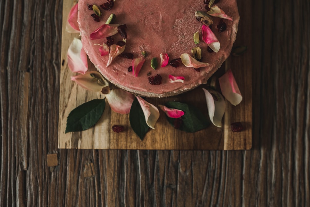 a cake with pink frosting and flowers on a cutting board