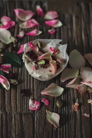 Delicate dessert of rose-flavored kulfi topped with pistachios and edible silver leaf on a ceramic dish.