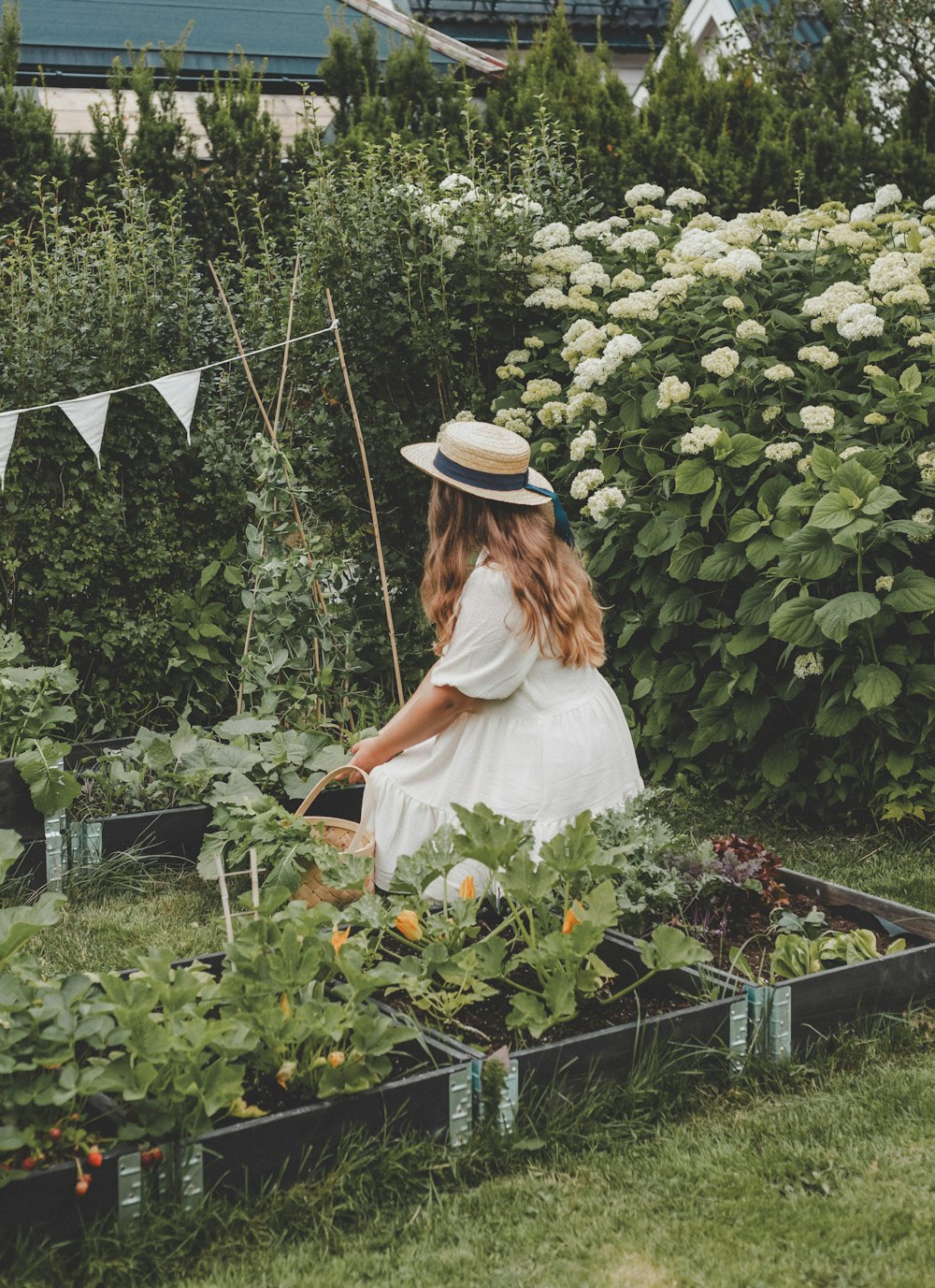 a woman in a white dress and hat tending to a garden