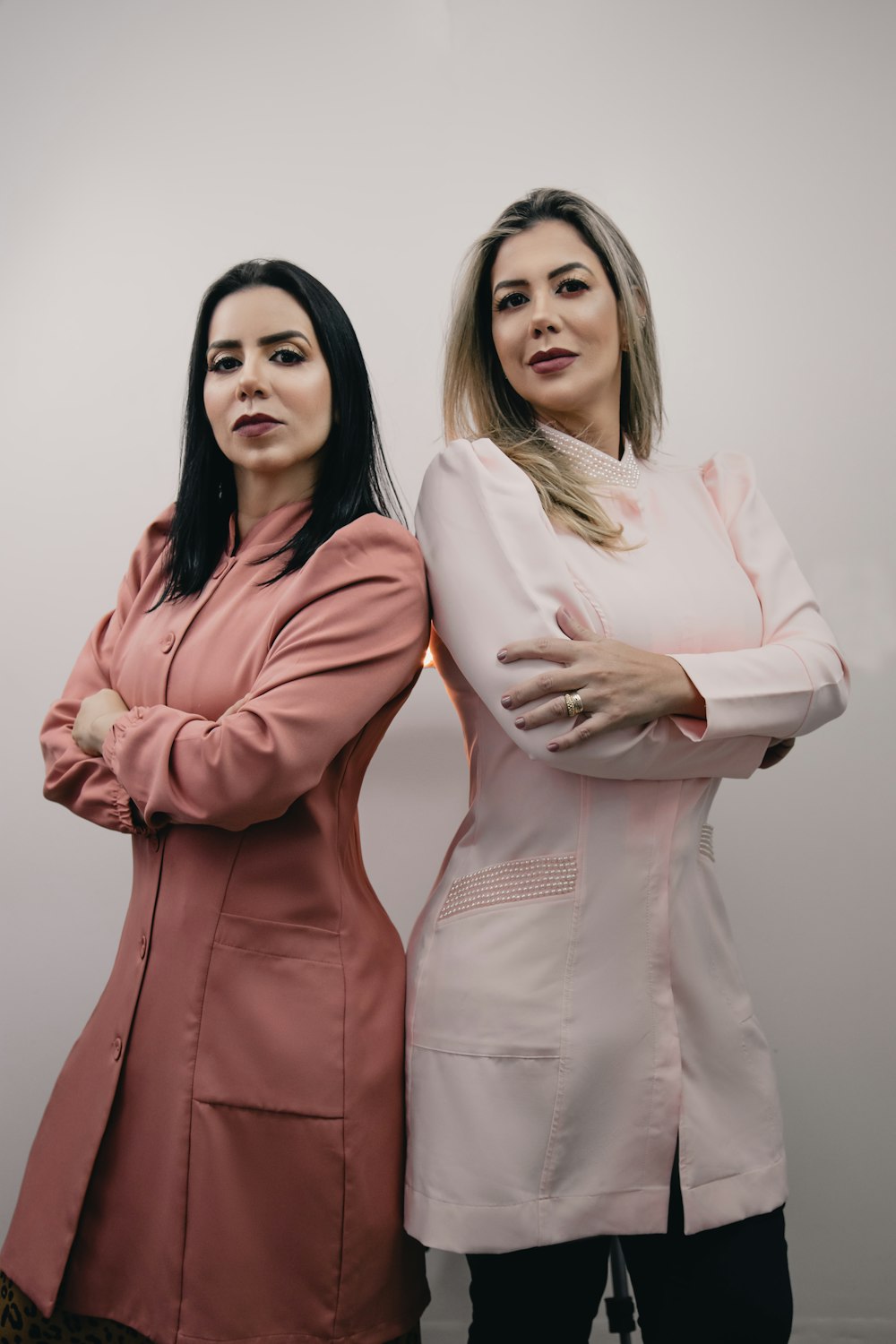 two women standing next to each other with their arms crossed