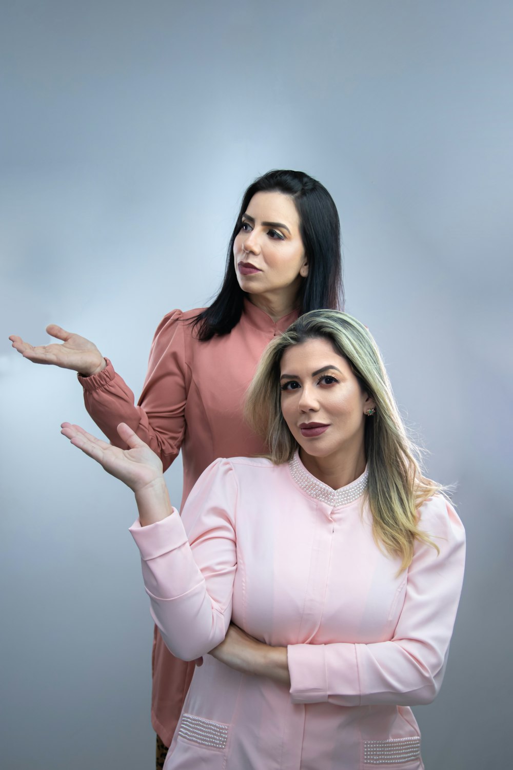 two women standing next to each other in front of a gray background