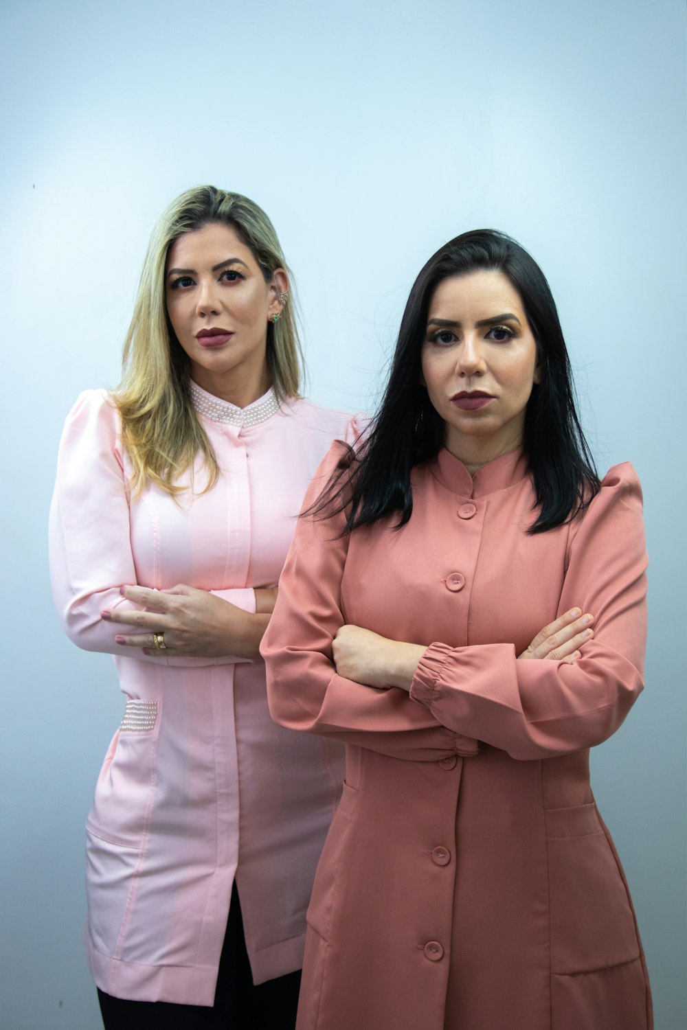 two women standing next to each other with their arms crossed