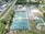 An aerial view of a sports complex featuring multiple tennis courts and a basketball court, surrounded by trees and a parking area with vehicles. There are paths leading to the courts, and a few small buildings nearby.