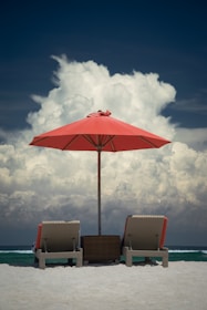 two lounge chairs under an umbrella on a beach