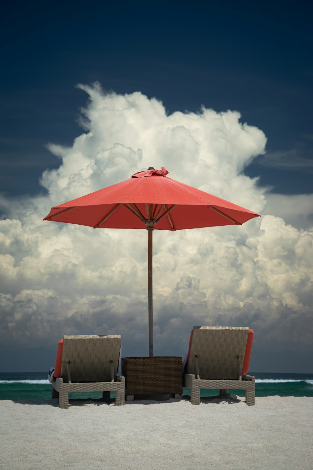 two lounge chairs under an umbrella on a beach