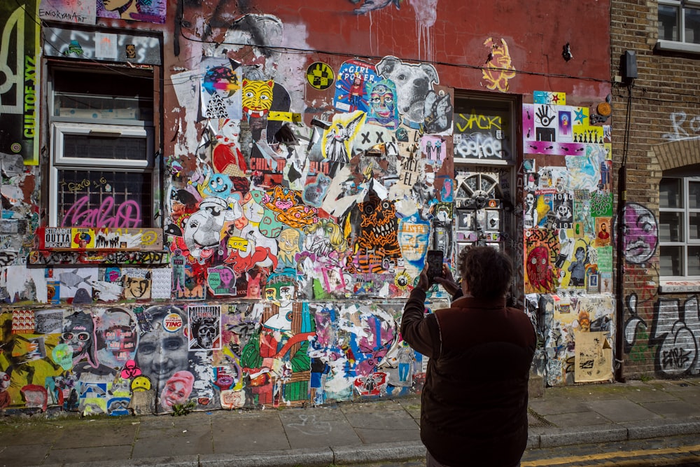 a woman taking a picture of a wall covered in graffiti
