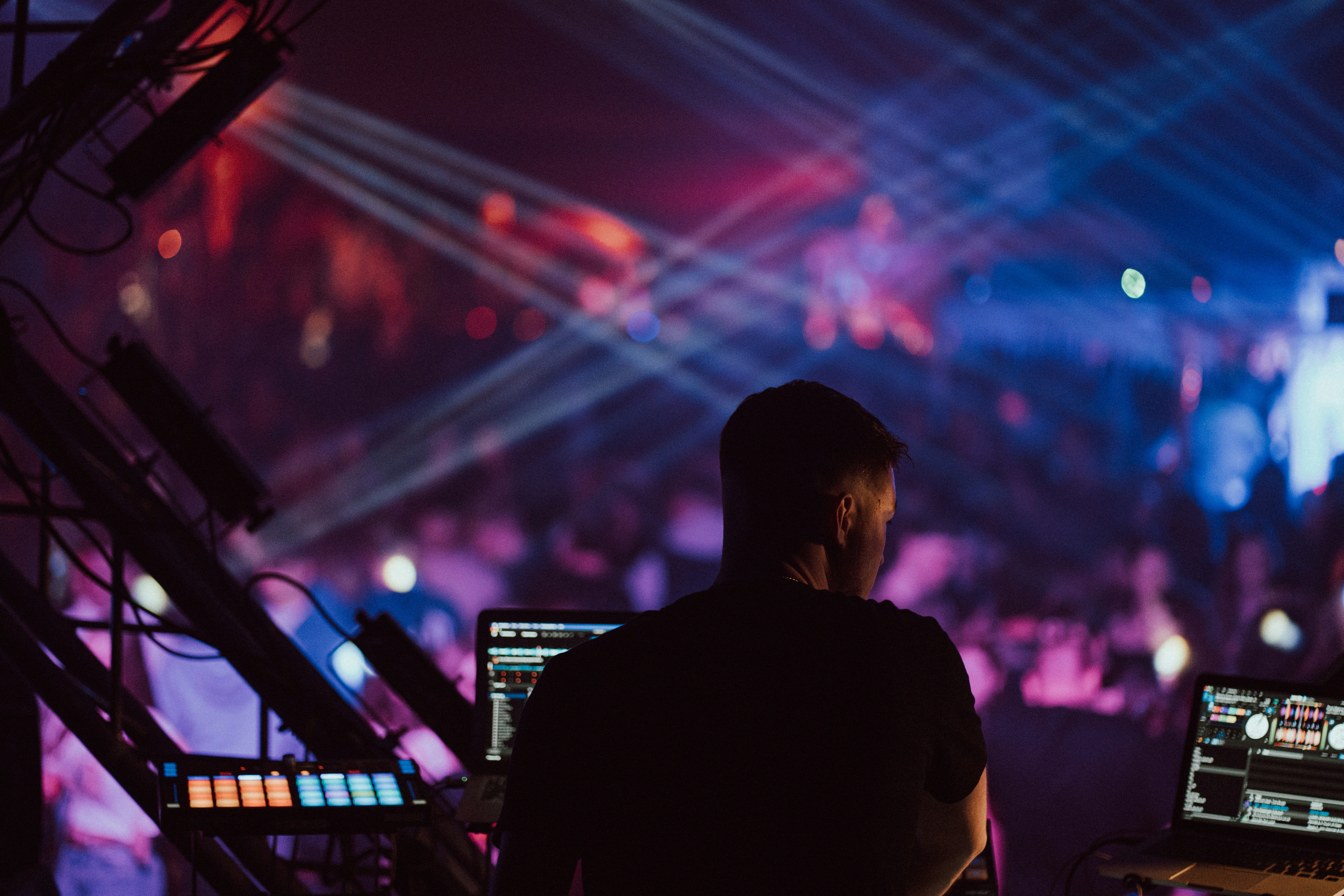 Wide shot of DJ on stage with purple and blue beam lights, large venue crowd