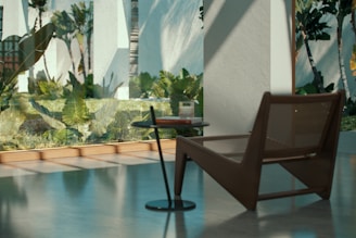 A modern interior space with large windows showcasing a lush green garden outside. The room features a minimalist design with a sleek brown lounge chair beside a small, round side table. Sunlight casts soft shadows across the polished concrete floor, enhancing the tranquil ambiance.