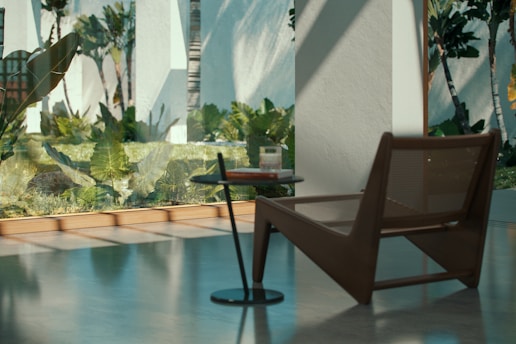 A modern interior space with large windows showcasing a lush green garden outside. The room features a minimalist design with a sleek brown lounge chair beside a small, round side table. Sunlight casts soft shadows across the polished concrete floor, enhancing the tranquil ambiance.