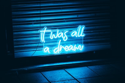 Neon blue text reading 'it was all a dream' is illuminated against a dark backdrop with metal shutters and tiled floor visible.