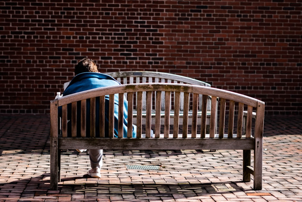 a person sitting on a wooden bench in front of a brick wall