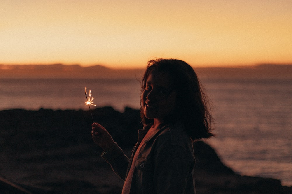 a woman holding a sparkler in front of a body of water