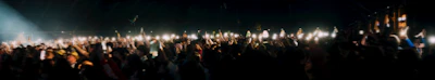 A lively concert crowd illuminated by neon lights and phone flashlights.