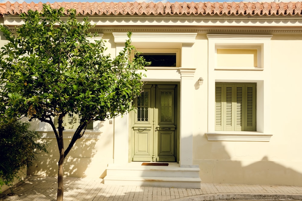 a white house with green shutters and a tree