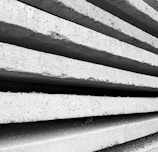 Rough concrete slabs are stacked closely on top of each other, showcasing their textured surfaces and industrial appearance. The perspective highlights the lines and shadows formed between the slabs.
