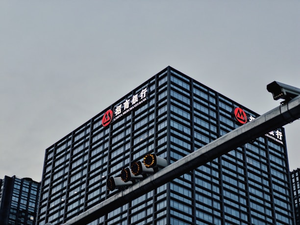 A tall, modern office building with a grid-like facade of windows is prominently visible. The logo and name 'China Merchants Bank' are displayed in white and red on the top of the building. In the foreground, there is a traffic light hanging on a metal pole.