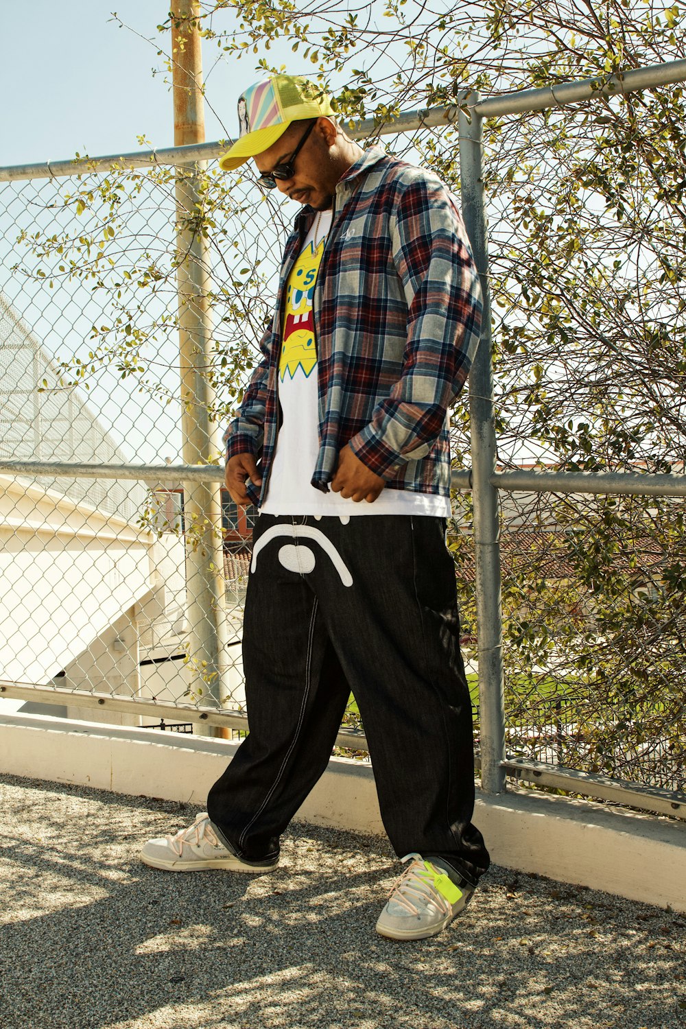 a man in plaid shirt and black pants standing next to a fence