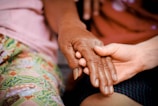 Hands of an elderly person and a child sharing ginguba in a warm, sunlit setting.