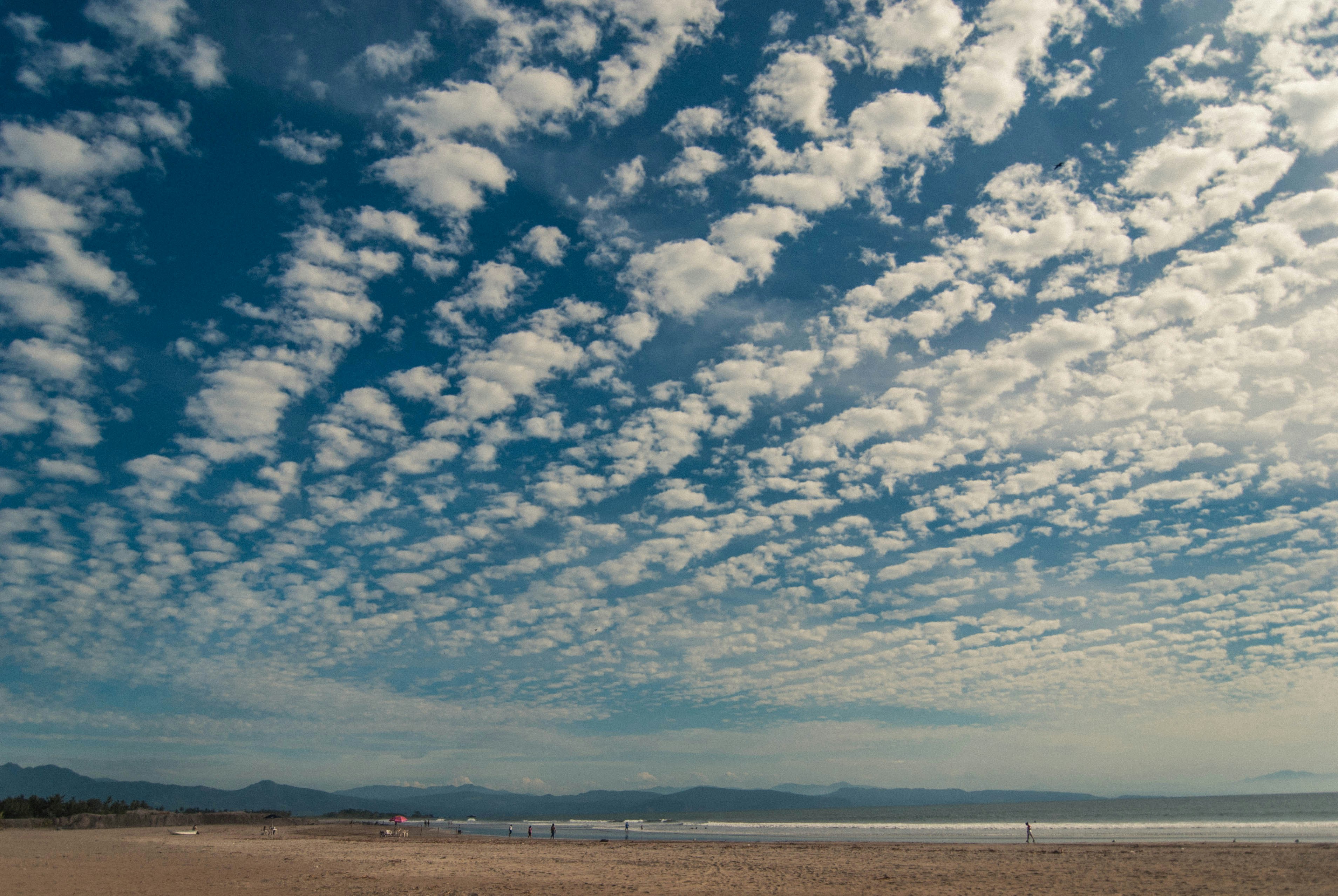 a group of people walking along a beach under a cloudy blue sky